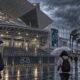 Illustrated visitors leave a Japanese gaming convention entrance in heavy rain.